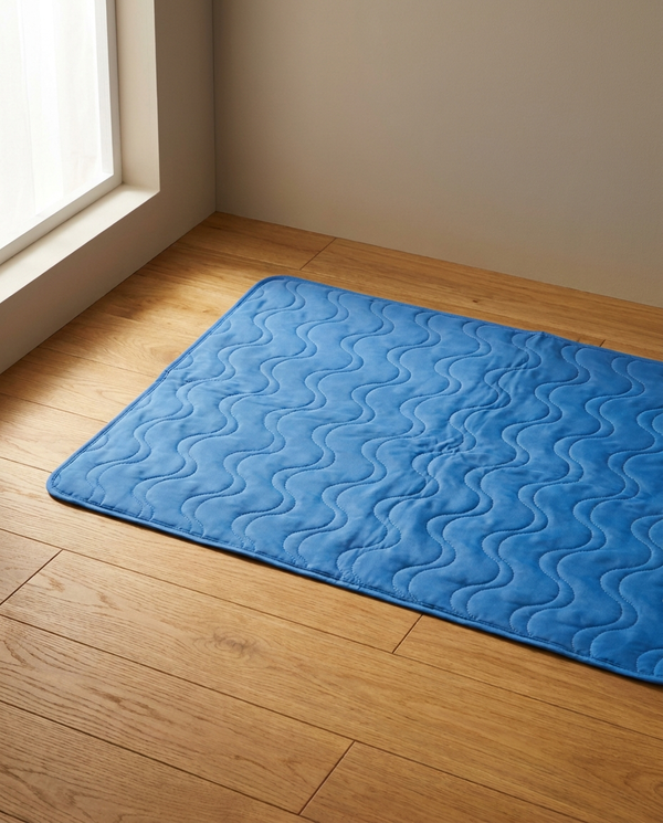 Blue quilted self-cooling dog gel mat laid flat on a warm oak wooden floor