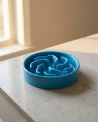 Bright blue slow-feed puzzle dog bowl clean and empty on a pale marble kitchen countertop