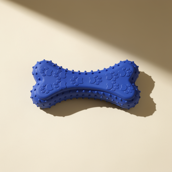 Buddies bite-resistant TPR dog chew bone in cobalt blue. Chunky rubber bone with paw-print embosses and bumpy nubs along the edge.