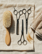 Overhead view of stainless steel dog grooming tools arranged on pale linen with a towel