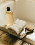 A bottle of dog shampoo on the edge of a bath beside a folded towel and grooming brush