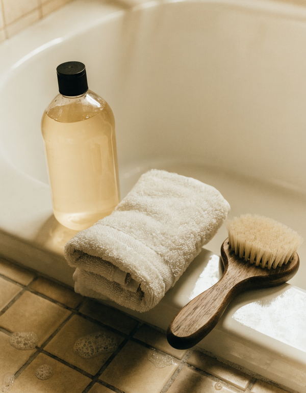 A bottle of dog shampoo on the edge of a bath beside a folded towel and grooming brush